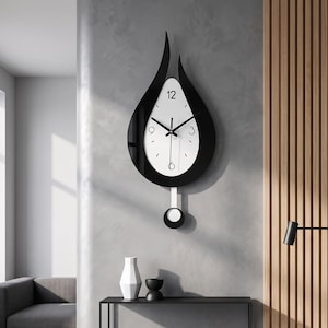 May include: A teardrop-shaped wall clock featuring a glossy black outer frame and a white center dial. The clock face displays black numerals at the 12, 3, 6, and 9 positions with thin black hands. A pendulum with a circular weight hangs below.