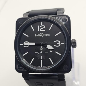 Puede incluir: Un reloj de pulsera con caja cuadrada negra y esfera negra que presenta el logotipo de Bell & Ross, n&uacute;meros ar&aacute;bigos blancos en las 12 y las 3, e &iacute;ndices de bast&oacute;n blancos. El reloj incluye una subesfera en la posici&oacute;n de las 6, manecillas blancas y una correa de caucho negra.