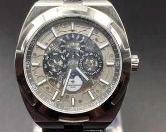 Könnte beinhalten: Eine silberfarbene Armbanduhr mit skelettiertem Zifferblatt, schwarzem Lederarmband, Mondphasenanzeige und mehreren Hilfszifferblättern für Wochentag, Datum und Monat. Auf dem Zifferblatt steht der Text Vacheron Constantin Geneve.