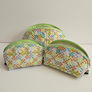 May include: Three semi-circular quilted pouches in varying sizes, featuring a colorful checkered pattern in pastel shades of yellow, blue, pink, and green. Each pouch has a bright lime green zipper closure and a soft, padded fabric construction.