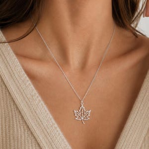Op de afbeelding: Een zilverkleurige ketting met een delicaat, opengewerkt esdoornblad-hangertje aan een dunne, bijpassende ketting. De hanger toont een gedetailleerd, uitgesneden aderpatroon over de hele bladvorm, wat zorgt voor een lichte en luchtige uitstraling.