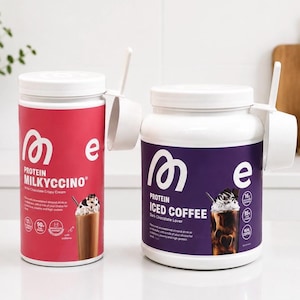 Könnte beinhalten: Zwei Protein-Pulver-Behälter mit weißen Deckeln. Einer ist rot mit "PROTEIN MILKYCCINO" und einer Grafik eines Schokoladengetränks. Der andere ist lila mit "PROTEIN ICED COFFEE" und einer Schokoladengetränk-Grafik. Beide haben einen weißen Messlöffel.