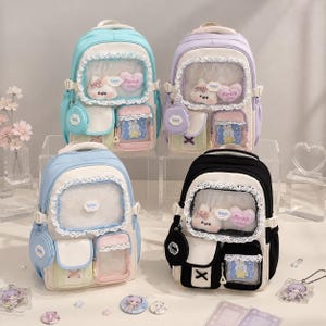 May include: Four backpacks in light blue, lavender, sky blue, and black, each featuring a clear front pocket with white lace trim, plush bunny and heart-shaped 'Barbie Girl' patches, side pouches, and smaller front compartments with clear windows.