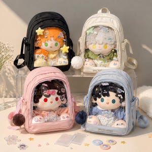 Könnte beinhalten: Vier Rucksäcke in Schwarz, Creme, Rosa und Hellblau, jeweils mit einer durchsichtigen Vordertasche, in der eine Plüschpuppe zu sehen ist. Die Puppen haben unterschiedliche Haarfarben und Outfits, verziert mit kleinen Stern- und Tieransteckern.