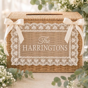May include: A rectangular light brown woven wicker box featuring a slot on top. The front is decorated with a white lace border and two cream-colored satin bows. The center displays the white text The HARRINGTONS printed on a clear panel.
