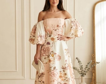 May include: An off-the-shoulder midi dress in a soft peach and cream color palette, featuring voluminous puff sleeves and a floral print with various blossoms. The dress has a fitted bodice and a flared skirt, paired with a small, solid cream clutch.
