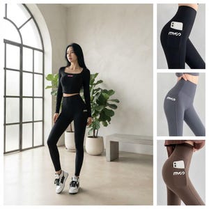 May include: A long-sleeve black crop top and high-waisted leggings set. The leggings feature a side pocket with the white text "mycs" printed on the pocket. The set is shown in black, gray, and brown, with a smartphone tucked into the side pocket.