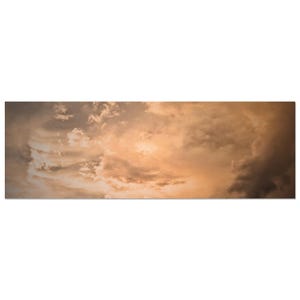 Op de afbeelding: Een panoramische, rechthoekige wandprint met een dramatische lucht vol zachte, ijle wolken verlicht door een warme, gouden zonsondergang. Het tafereel verloopt van lichte amberkleurige tinten in het midden naar diepe, schaduwrijke grijze wolken.