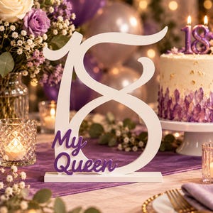 Peut inclure: Un centre de table en bois blanc en forme de chiffre 18 avec le texte en écriture violette My Queen fixé sur le devant. L'objet repose sur une base rectangulaire blanche et est conçu pour être posé sur une surface plane pour un dix-huitième anniversaire.