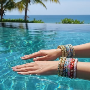 Peut inclure: Une collection de bracelets joncs en métal empilés avec des finitions en émail coloré et des motifs floraux complexes. Les bracelets sont présentés dans diverses teintes dont le rouge, le bleu, le rose et l'or, avec des détails décoratifs.