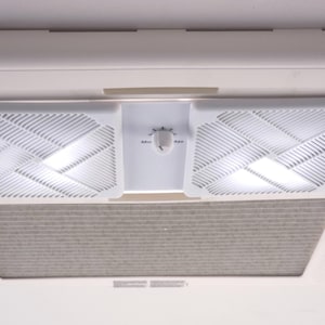 Peut inclure: Une unité de ventilation de plafond rectangulaire blanche dotée de deux grilles carrées à motif de lattes géométriques. Un panneau de commande central comprend un bouton circulaire unique marqué des réglages Min et Max. Un filtre gris est visible.