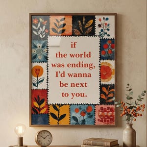 May include: A framed artwork with a floral patchwork design and the text "if the world was ending, I'd wanna be next to you." The artwork is displayed on a wooden table with a lamp, clock, and books.