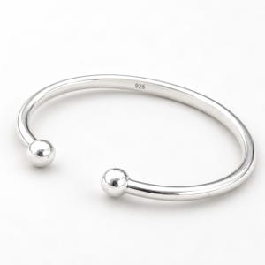May include: A polished silver cuff bracelet with a smooth, open-ended design featuring a spherical ball at each end. The inner surface of the metal band is clearly stamped with the text 925, indicating the sterling silver composition of the piece.