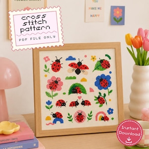 May include: A framed cross stitch pattern featuring a collection of red and black ladybugs in various poses, including flying, resting on flowers, and crawling on leaves, set against a white fabric background with small colorful decorative elements.