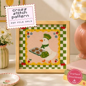 May include: A cross stitch pattern PDF file featuring a white duck wearing a green chef hat and scarf, holding a tray of cookies. The design includes a pink center, a yellow scalloped border, and a green and white checkered frame with cherries.