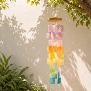 May include: A hanging wind chime featuring a circular wooden top and multiple strands of translucent, colourful, square and circular discs in a gradient pattern of purple, pink, orange, yellow, green, and blue, suspended by a metal chain.