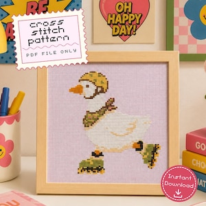 May include: A cross stitch pattern featuring a white goose wearing a yellow helmet, a green patterned scarf, and green roller skates. The design is set against a light purple background and framed in a light wood frame. Text reads cross stitch pattern.