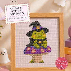 Puede incluir: Un patrón de punto de cruz en archivo PDF que muestra una rana verde con un sombrero de bruja negro y banda morada, sentada sobre una seta morada con puntos blancos. Enmarcado en madera clara. Texto: cross stitch pattern PDF FILE ONLY.