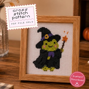 Puede incluir: Un patrón de punto de cruz en archivo PDF que muestra una rana verde con sombrero y túnica de bruja negra, sosteniendo una varita con punta de estrella naranja. El diseño está en un marco de madera clara con el texto cross stitch pattern PDF FILE ONLY.
