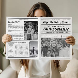 May include: A black and white wedding newspaper with the headline "Emily, Will You Be My Bridesmaid?" and photos. The design includes a bridesmaid word search and wedding details. The paper is held up by a person, with the text visible.