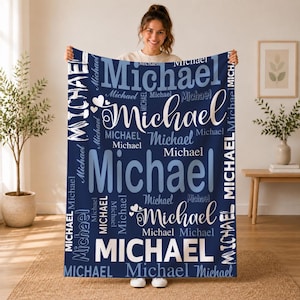 May include: A navy blue fleece blanket featuring the name Michael printed repeatedly in various white and light blue fonts, sizes, and orientations, accented with small heart graphics throughout the design for a personalized look.