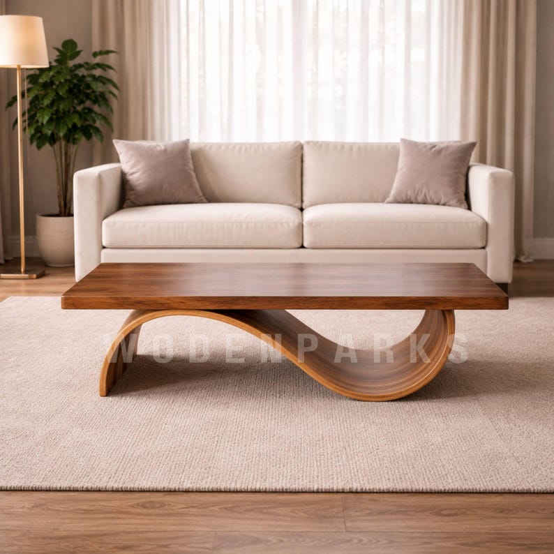 Op de afbeelding: Een moderne salontafel van massief hout met een unieke, gebogen basis. Het tafelblad is een rijk, donkerbruin en de basis heeft een lichtere houttint. De tafel staat in een woonkamer met een cr&egrave;mekleurige bank en een neutraal tapijt.