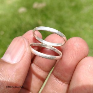 May include: Two plain, polished silver bands with a smooth, rounded profile. These simple rings feature a consistent, minimalist circular shape and a bright, reflective metallic finish, showcasing a clean and unadorned design for everyday wear.