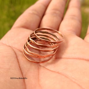 Könnte beinhalten: Ein Stapel dünner, kupferfarbener Ringe mit gehämmerten Strukturen. Die Ringe sind auf einer Hand gestapelt, mit einem verschwommenen grünen Hintergrund. Der Text "925SilverBohoGifts" ist unten links sichtbar.