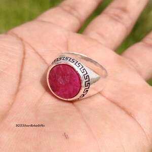 May include: A silver ring with a large, oval, deep red gemstone. The ring has a decorative border with a repeating geometric pattern. The ring is held in a hand, with the text "925SilverBohoGifts" visible.