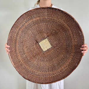 Könnte beinhalten: Ein großes, rundes und flaches geflochtenes Tablett mit einer dunkelbraunen, eng gewickelten Textur auf der gesamten Oberfläche. In der Mitte des Tabletts befindet sich ein kontrastierendes quadratisches Feld aus beigem Naturgeflecht.