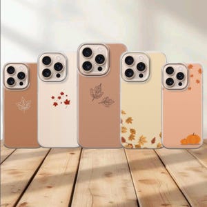 May include: Five smartphone cases in varying shades of tan, beige, and orange. Each case features a unique autumn-themed design, including line-art maple leaves, scattered fall foliage, and small orange pumpkins, all with a triple-lens camera cutout.