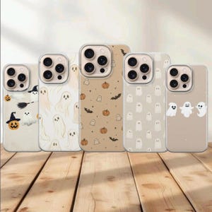 Op de afbeelding: Vijf smartphonehoesjes met Halloween-thema. De hoesjes tonen diverse patronen met geesten, pompoenen en vleermuizen in neutrale beige, crème en witte kleurenpaletten, elk voorzien van een uitsparing voor een camera met drie lenzen.