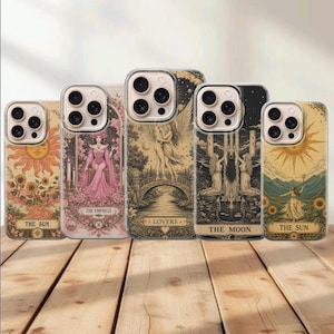 Könnte beinhalten: Fünf transparente Smartphone-Hüllen mit Tarotkarten-Illustrationen. Die Designs zeigen Die Sonne mit Sonnenblumen, Die Herrscherin in einem rosa Kleid, Die Liebenden auf einer Brücke, Der Mond mit Wölfen und ein zweites Motiv Die Sonne.