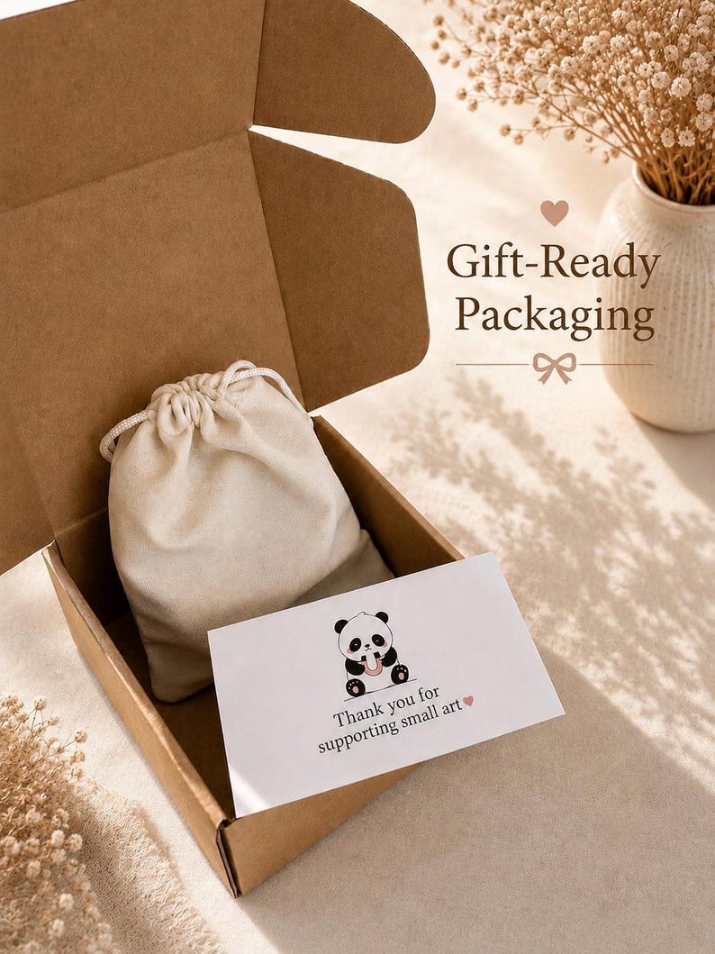 May include: A brown cardboard shipping box containing a cream-colored drawstring pouch and a white rectangular card. The card features a black and white panda illustration and the text: Thank you for supporting small art. The text Gift-Ready Packaging is visible.