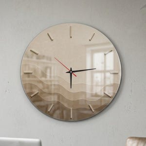 Puede incluir: Un reloj de pared circular con un diseño degradado de líneas onduladas horizontales en tonos beige y marrón. El reloj tiene una superficie lisa, manecillas negras finas para horas y minutos, un segundero rojo fino y marcas verticales.