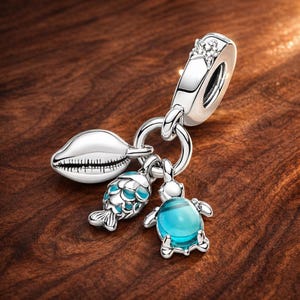 Puede incluir: Un charm de plata con una concha, un pez con escamas azules y una tortuga con un cuerpo de gema azul. El charm tiene un anillo y una parte superior decorativa con un pequeño diseño floral. El charm está sobre una superficie de madera.