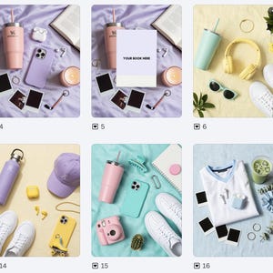 May include: A collection of items including a light pink tumbler, a purple phone case, white wireless earbuds, a candle, two blank polaroid-style frames, a gold ring, a keychain, and an open book on a light purple fabric surface.