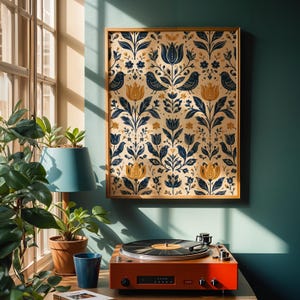 Op de afbeelding: Een rechthoekige wandkunstprint met een herhalend patroon van donkerblauwe vogels en goudgele tulpen op een crèmekleurige achtergrond, ingelijst in een dunne houten lijst. Het kunstwerk hangt aan een blauwgroene muur boven een rode platenspeler.