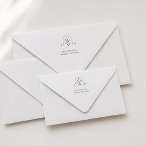 Peut inclure: Trois enveloppes blanches de tailles différentes avec un logo imprimé en noir comprenant une ligne arquée, un brin de feuille central, les lettres S et W, et l'adresse 128 Victoria St, Fitzroy, VIC 3065 en police serif sombre sur le rabat.