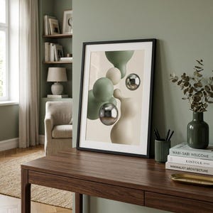 May include: A framed abstract art print with floating shapes in green, cream, and silver. The black frame sits on a dark wood desk, with books, a vase, and a pencil holder. The artwork is a modern home decor piece.