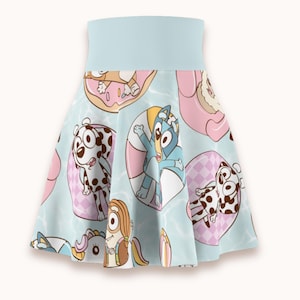 May include: A light blue skater skirt featuring an all-over print of cartoon dogs in pink and white inflatable pool rings. The skirt has a wide, solid light blue waistband and a flared silhouette with various animated characters in swimming gear.
