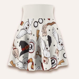 May include: A cream-colored skater skirt featuring a repeating pattern of white owls, black witch hats, brown broomsticks, gold lightning bolts, round glasses, winged keys, striped scarves, and circular signs that read Platform 9 3/4.