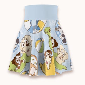 May include: A light blue skater skirt featuring a repeating pattern of cartoon dogs in pool floats, beach balls, and a green dinosaur float. The skirt has a wide, solid light blue waistband and a flared silhouette with a water-like background.