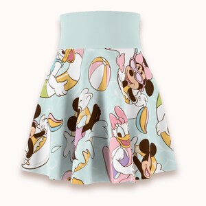 Puede incluir: Una falda skater de color azul claro con un estampado integral de personajes de dibujos animados, incluyendo a Mickey Mouse, Minnie Mouse y Daisy Duck, disfrutando de un día de playa con pelotas y flotadores, con una cintura ancha y lisa.