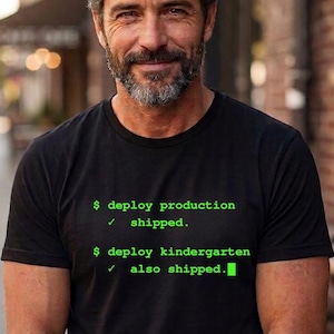 Könnte beinhalten: Schwarzes T-Shirt mit grünem Text: "$ deploy production ✓ shipped. $ deploy kindergarten ✓ also shipped." Das T-Shirt wird von einer Person mit Bart getragen.