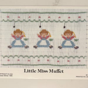 May include: A printed image featuring three smocked figures of Little Miss Muffet, each with blonde hair, a blue dress, and red accents. The design is set against a light blue background with green and pink floral patterns. The text "Little Miss Muffet" is displayed.