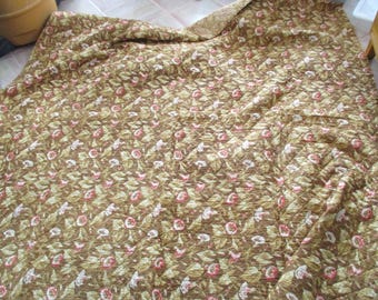 Può includere: Un copriletto trapuntato con un motivo ripetuto di foglie marroni e piccoli fiori rosa e bianchi. Il tessuto presenta una superficie testurizzata e cucita, con un angolo ripiegato che rivela un motivo coordinato sul retro in tonalità simili.