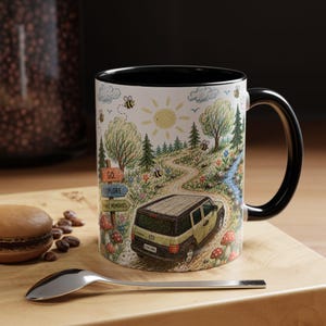 May include: White ceramic mug with a black interior and handle. The mug features a colourful illustration of a road winding through a forest, a yellow SUV, bees, and the words "GO", "EXPLORE", and "MAKE MEMORIES".