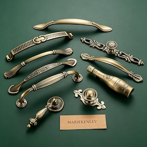 May include: A collection of antique brass-toned metal cabinet pulls and knobs in various shapes, including a bottle-shaped handle, alongside a rectangular card with the text MARIEKENLEY printed in black on a light brown background.