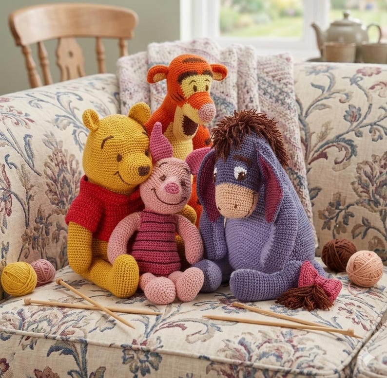 May include: A collection of handmade crochet Winnie the Pooh characters, including Winnie, Piglet, Tigger, and Eeyore. Winnie wears a red shirt, Piglet a pink striped shirt, and Eeyore a purple body. The toys are arranged on a floral patterned couch.